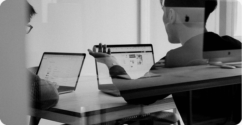 Two people sitting at a desk collaborating while working on laptops in a modern office