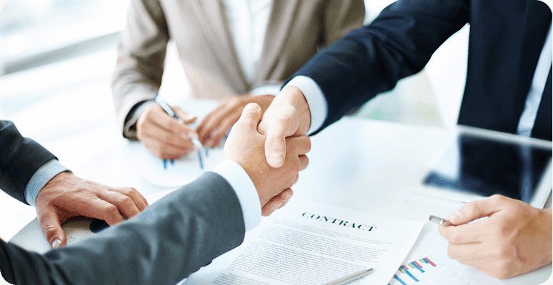 Two people in business attire shake hands across a table.