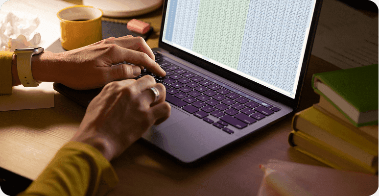 Hands typing on a laptop displaying a spreadsheet