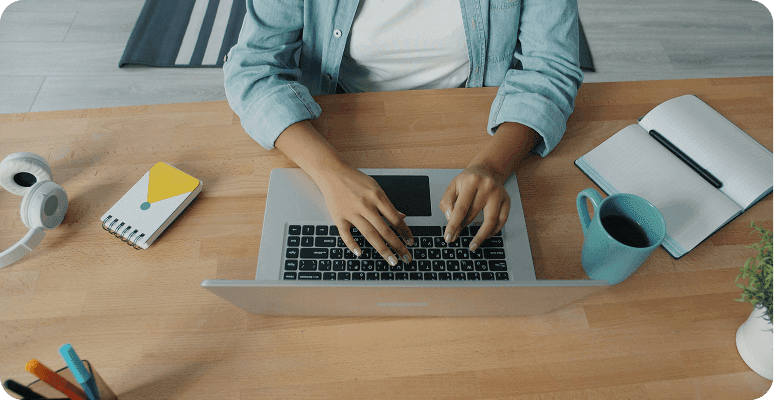 Top-down view of hands typing on a laptop at a desk