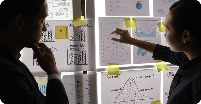 Two people discussing charts and data displayed on a wall