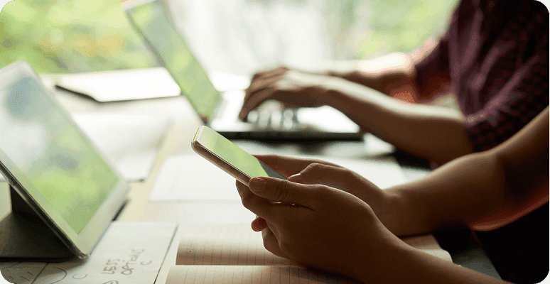 Person using a smartphone with laptop and tablet in the background