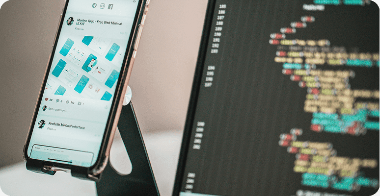 Smartphone displaying a UI design next to a computer screen with code
