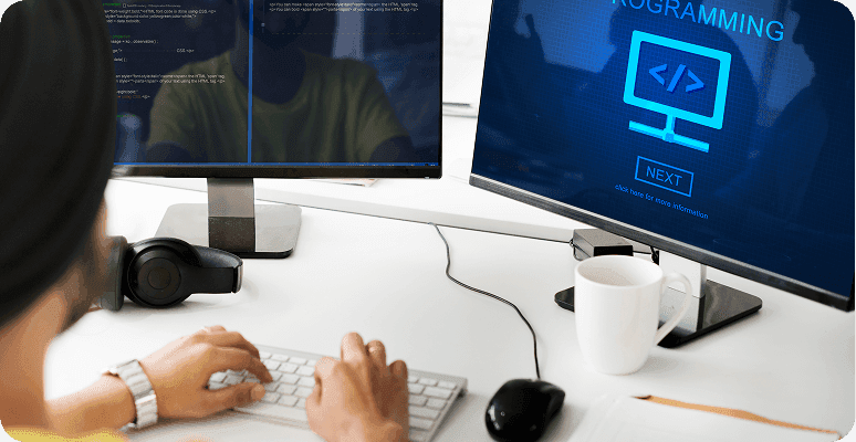 Person coding on a computer with a programming graphic on a second screen