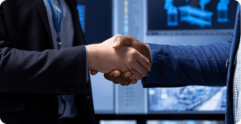 Two business professionals shaking hands in front of a computer screen, symbolizing partnership or agreement.