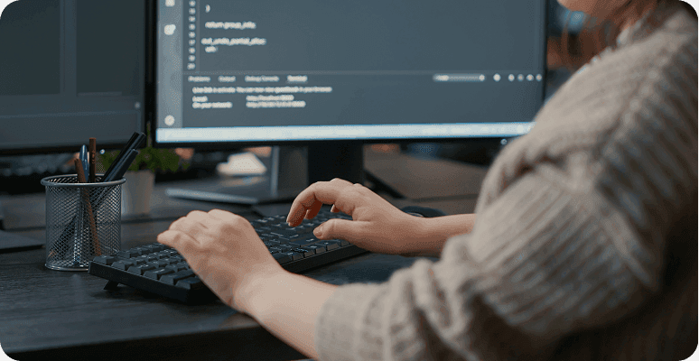 Hands typing on a keyboard in front of a coding screen